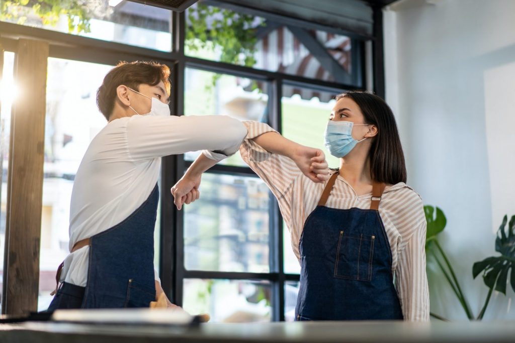 Asian waiter worker greeting waitress girl by elbow bump in restaurant.